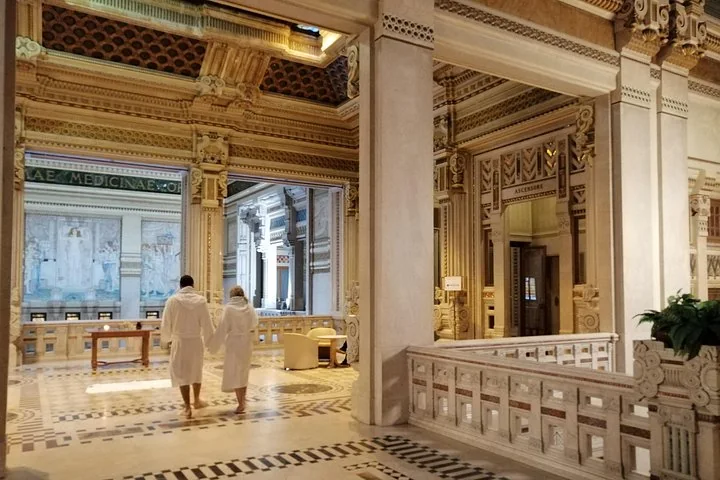 Zwei Personen in weißen Bademänteln gehen durch eine Marmorhalle mit prunkvoller Dekoration im Liberty-Stil