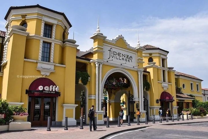 Gelbe Gebäude im Liberty-Stil mit kleinen Türmen rund um ein Bogentor und ein Café mit roter Markise